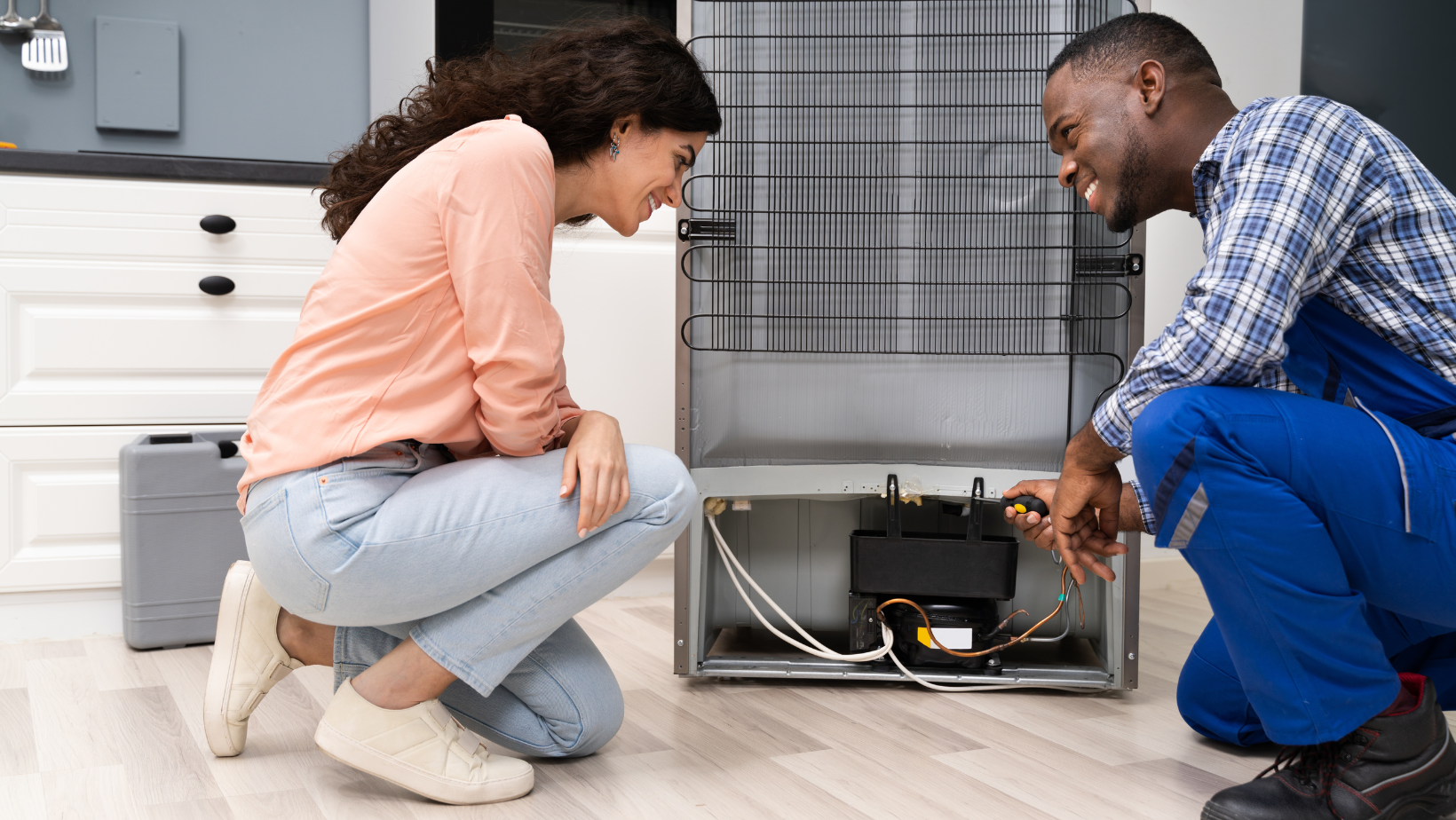 A man and woman looking at the back of the fridge.